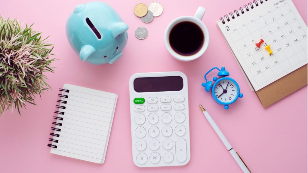 budgeting tools to save money: a calculator, calendar, piggy bank, money, notebook, and pen