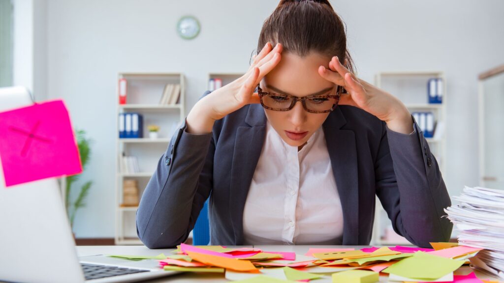 woman sitting at desk with hands on temples surrounded by a stack of notes
