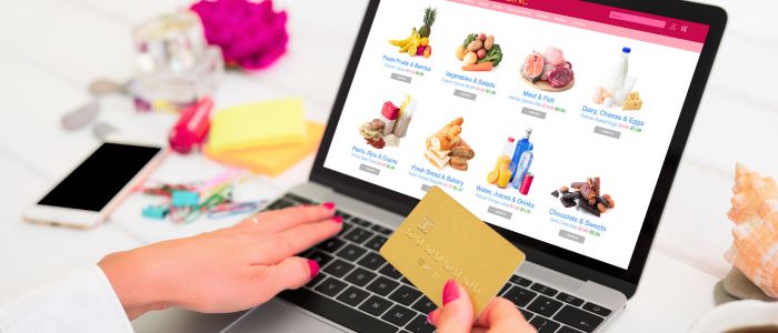 fh-inblog-person-grocery-shopping-online (1) a person holding a credit card while shopping online for groceries using a laptop