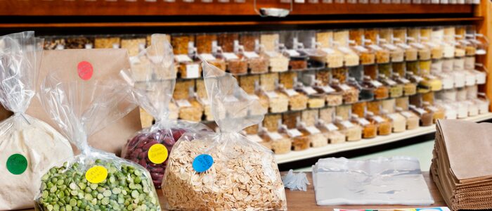 fh-inblog-bulk-grains-beans-store Bulk food bins filled with grains, beans, oats, and dry goods in a refill-style grocery store with paper bags and plastic scoops