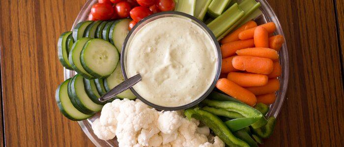 fh-inblog-precut-veggie-tray Pre-cut vegetable tray with baby carrots, celery sticks, cherry tomatoes, cucumber slices, cauliflower, green bell pepper, and ranch dip in the center