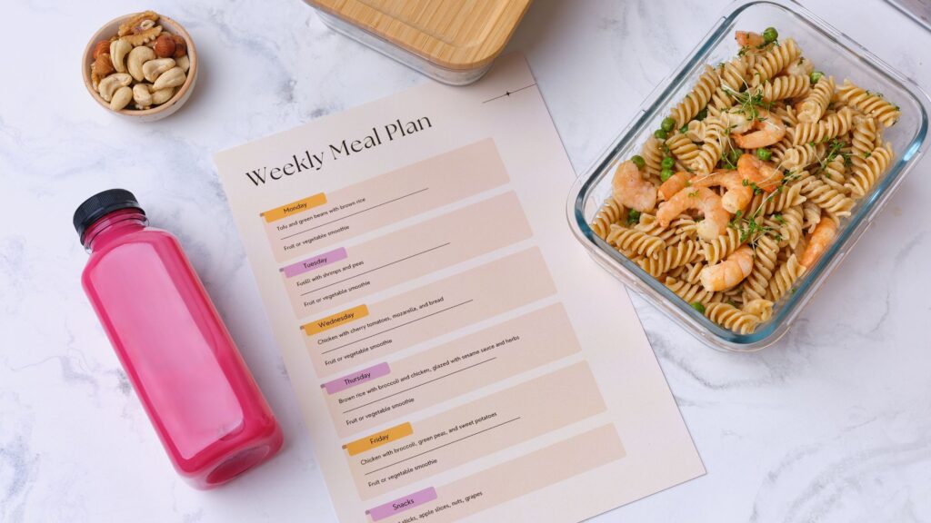 Weekly meal plan with a glass container of shrimp pasta, a pink smoothie, and a bowl of mixed nuts.