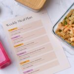 Weekly meal plan with a glass container of shrimp pasta, a pink smoothie, and a bowl of mixed nuts.