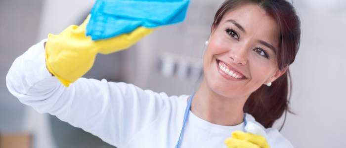 Smiling person cleaning with yellow gloves and a blue cloth, showing how simple habits make living frugally rewarding.