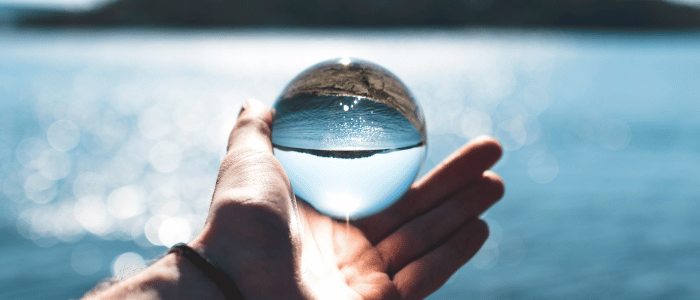 close-up of a person holding a clear, glass globe reflecting the lake blurred in the backdrop