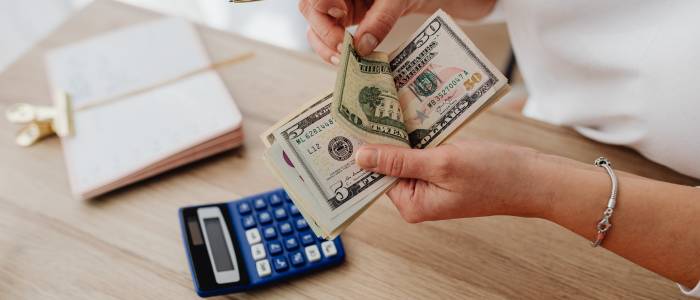 Hands counting cash at a desk with a calculator and notebook.