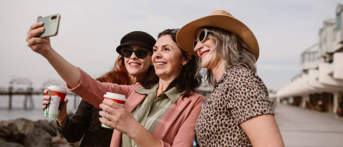 Three smiling women taking a selfie outdoors while holding coffee cups, representing friendship, happiness, and the simple rewards of frugal living.