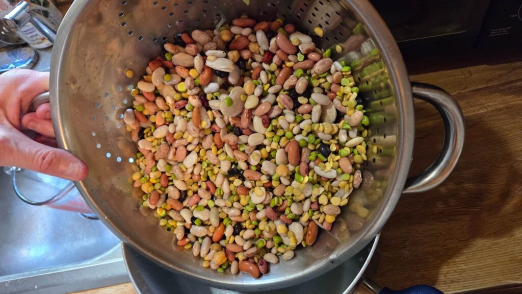 Rinsed mixed beans and lentils in a metal colander on a kitchen counter, representing simple, intentional frugal cooking at home.