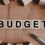 Wooden blocks spelling “BUDGET” on a desk surrounded by office supplies, representing planning and money management.