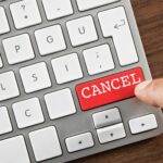 Close-up of a computer keyboard with a red “CANCEL” key being pressed by a finger