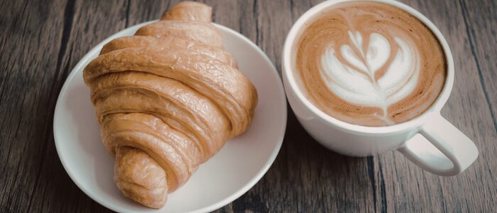 fh-inblog-morning-coffee Croissant on a white plate with a latte featuring heart-shaped foam, representing everyday spending like coffee and breakfast.