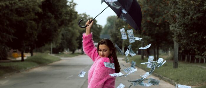 Person holding an umbrella outdoors while paper money falls around them in the air