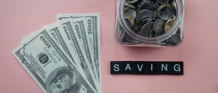 US dollar bills and a jar of coins next to the word “saving,” representing building savings over time