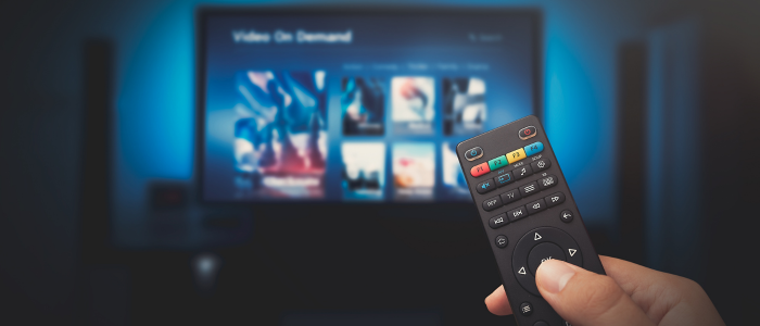 Hand holding a TV remote aimed at a streaming service interface on a television screen