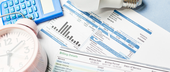 Household bills beside a calculator, alarm clock, and light bulb on a desk.
